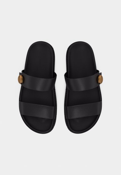 Μαύρα σανδάλια τύπου slip-on με δύο φαρδιές λουριά και στρογγυλά χρυσά κουμπιά στις εξωτερικές πλευρές, παρουσιάζονται σε λευκό απλό φόντο.