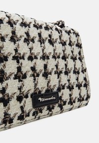 Gros plan d’un sac à main tissé noir et blanc à motif pied-de-poule avec une étiquette de marque Tamaris argentée et une bandoulière chaîne argentée.