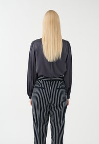 Svart långärmad blus med mjuk textur, kombinerad med navy och vitrandiga högmidjade byxor med fickor och en skräddarsydd passform.