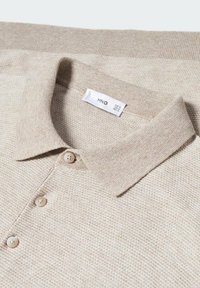 Polo de punto beige con cuello doblado, tres botones a juego y etiqueta de la marca visible dentro del cuello.