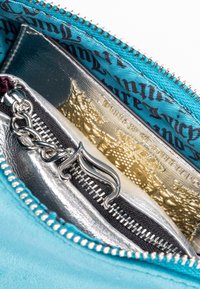 Interno della borsa in suede teal con fodera argentata, dotato di più scomparti con zip e un accento decorativo in metallo.