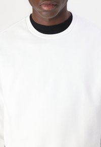 Vit sweatshirt med rund halsringning och ribbad svart innerkrage. Slät textur, inga synliga mönster eller dekorationer.