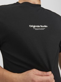 Schwarzes Baumwoll-T-Shirt mit kurzen Ärmeln. Verfügt über ein weißes, aufgedrucktes Logo "Originals Studio" auf der linken Brust. Weicher Stoff, taillierte Passform.