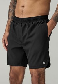 Black swim shorts made of lightweight fabric with an elastic waistband, side pockets, and a small logo accent on the lower leg.