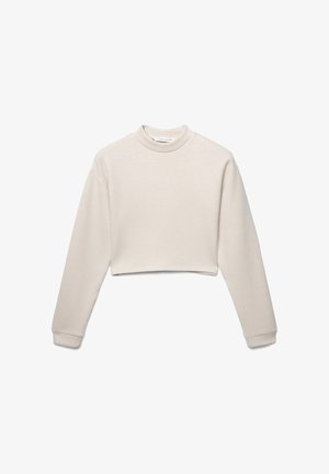 Sk cropped bluzie w jasnym beżu, wykonaną z miękkiego materiału. Posiada długie rękawy, wysoki dekolt i ribbowe mankiety. Bez widocznych wzorów.