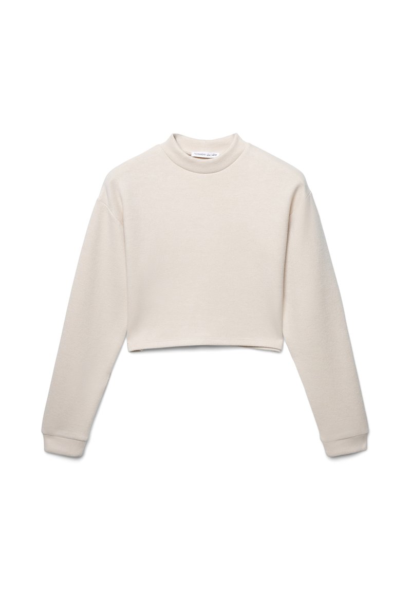 Sk cropped bluzie w jasnym beżu, wykonaną z miękkiego materiału. Posiada długie rękawy, wysoki dekolt i ribbowe mankiety. Bez widocznych wzorów.