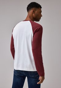 T-shirt a maniche lunghe con corpo bianco e maniche raglan bordeaux. Design con collo rotondo, realizzato in morbido tessuto di cotone, con orlo dritto.