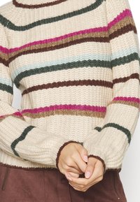 Stickad tröja i krämfärg med horisontella ränder i grönt, rosa, brunt och ljusblått; ribbade ärmmuddar och rund halsringning.