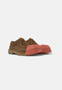 Brown leather shoes with a rounded pink rubber toe cap. Features laces and a textured outsole for grip. Modern design and durable materials.