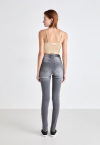 Gray high-waisted skinny jeans with a smooth texture, paired with a beige cropped top featuring a woven back and adjustable straps.