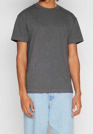 Man wearing a dark gray short-sleeve t-shirt and light blue jeans, standing against a plain light background.