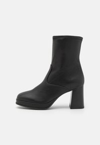 Botte en cuir noire mi-mollet avec bout arrondi, talon carré et coutures sur la surface lisse, présentée sur un fond blanc uni.