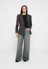 Μαύρο σακάκι με διπλό πέτο και ρίγες, εφαρμοστό μαύρο τοπ, ανοιχτό γκρι τζιν με φαρδιά μπατζάκια και μπορντό τσάντα χειρός. Το σύνολο χαρακτηρίζεται από κομψές υφές.