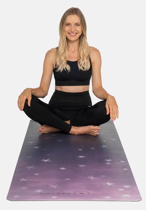 Yogamat in een vervagende paarse tint met sterrenpatronen. Gebruiker zit in kleermakerszit, gekleed in zwarte sportkleding, blote voeten op de mat.
