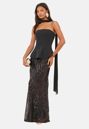 Black strapless peplum top paired with a sequined black skirt featuring wavy patterns. Model holds a silver clutch, accented with a black scarf.