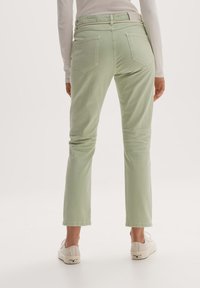 Pantaloni corti verde chiaro con vita alta, due tasche posteriori e una texture morbida, abbinati a scarpe di tela bianche.