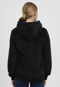 Fuzzy black hoodie with a large hood, textured fabric, ribbed hem and cuffs, and a relaxed fit. No visible branding.