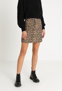 Minirock aus Leoprint-Denim mit fransigem Saum, hoher Taille und Knopfverschluss vorne, kombiniert mit einem schwarzen, strukturierten Pullover und schwarzen Stiefeletten.