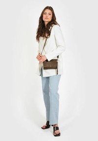 Borsa a tracolla in pelle marrone con superficie texturizzata, hardware in argento e cinturino regolabile, indossata con un blazer bianco e jeans in denim chiaro.