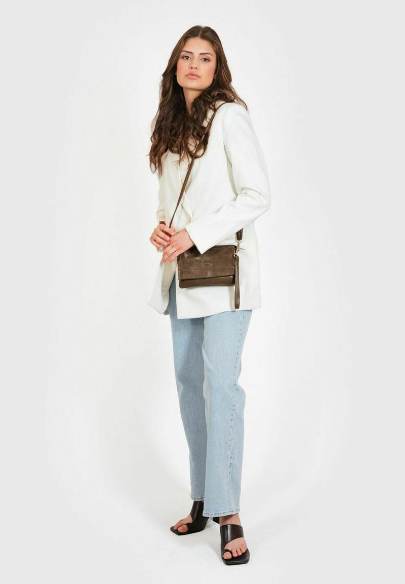 Borsa a tracolla in pelle marrone con superficie texturizzata, hardware in argento e cinturino regolabile, indossata con un blazer bianco e jeans in denim chiaro.