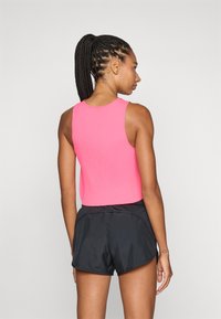 Rosa geripptes Crop-Top, ärmelloses Design, kombiniert mit schwarzen Sportshorts. Glatte Textur, figurbetonte Silhouette, minimale Details.