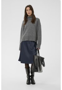 Pull en tricot gris à col montant, jupe en satin bleu marine, sac fourre-tout en cuir noir et bottes de cow-boy noires. Textures lisses et coupe décontractée.