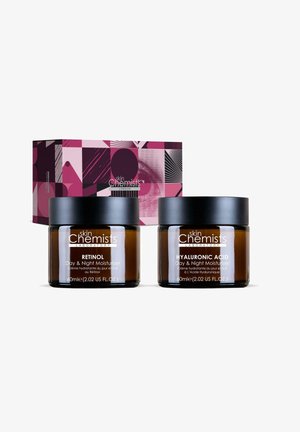 Two 60ml amber glass jars with black lids of Skin Chemists retinol and hyaluronic acid day & night moisturizers in front of a patterned pink product box.