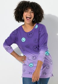 Paarse lange mouwen shirt met glimlachende gezichtenpatronen in lichtblauw, met een ontspannen pasvorm en een ronde halslijn. Draagt over denim.