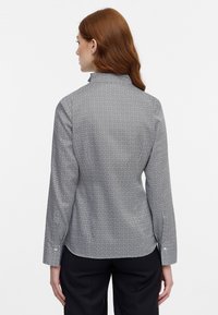 Collared blouse in navy with a geometric pattern, long sleeves, and buttoned cuffs. Smooth fabric with a tailored fit and mid-length hem.