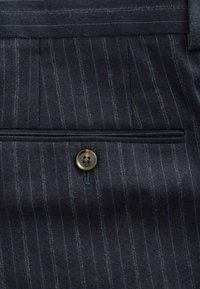 Navy striped fabric with visible texture, featuring a single button closure and pleats. Soft wool blend with a refined finish.