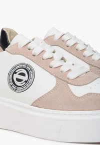 Bílé tenisky se růžovým semišovým akcentem, texturovanými tkaničkami, kulatou nášivkou s logem a silnou bílou gumovou podrážkou.