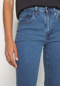 Jeans di denim blu con vestibilità slim, dotati di cinque tasche, una vita standard e sottili dettagli di cucitura. Tessuto strutturato con una finitura liscia.
