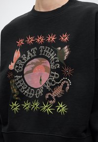 Μαύρο φούτερ με κεντημένη σκηνή ερήμου, σκορπιό, κολίβρι και το κείμενο "Μεγάλα πράγματα μπροστά σου", περιτριγυρισμένο από λουλουδάτα μοτίβα.