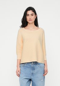 Ανοιχτό ροδακινί ριμπ πουλόβερ με φαρδύ λαιμόκοψη και μανίκια τριών τετάρτων, συνδυασμένο με τζιν παντελόνι σ ε ανοιχτό μπλε χρώμα με σκισίματα.