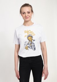 Bílý bavlněný tričko s grafickou ilustrací medvěda na motorce s medvídětem, s černým a žlutým textem vytištěným nahoře.