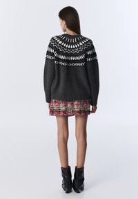 Maglione grigio lavorato a maglia con un colletto a motivo bianco e nero, abbinato a una gonna a quadri rossa e stivali neri alla caviglia. Vista da dietro.