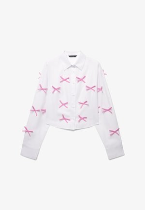 Chemise blanche à manches longues, coupée, avec des accents de ruban rose en motif 'X' sur le devant et les manches.