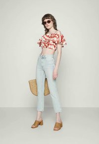 Top cropped às riscas vermelhas e brancas com mangas bufantes, jeans justos azul claro, sandálias de salto trançadas em tom castanho e uma bolsa redonda em palha.