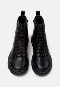 Une paire de bottes montantes en cuir noir avec des zips sur les côtés et des lacets noirs, présentée vue du dessus sur un fond gris.