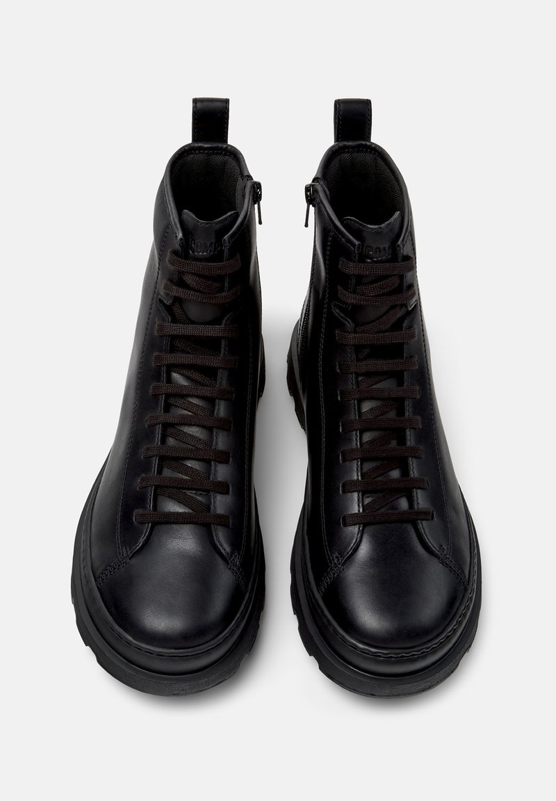 Ein Paar schwarze Lederhohe Stiefel mit seitlichen Reißverschlüssen und schwarzen Schnürsenkeln, von oben auf einem grauen Hintergrund gezeigt.