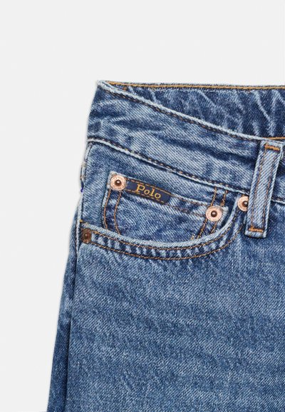 Κοντινή λήψη μπλε τζιν με μπροστινή τσέπη, χάλκινα καρφιά, θηλιά για ζώνη και μικρή ετικέτα "Polo" στην άκρη της τσέπης.
