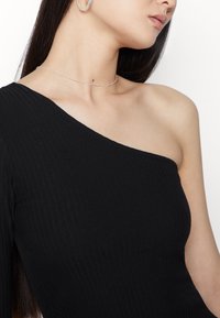Schwarzes, geripptes Top mit einem Schulterdesign. Hat eine glatte Textur und eine enganliegende Form. Trägt eine dünne silberne Choker-Halskette.