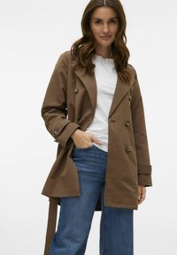 Brun dubbelknäppt trenchcoat med bälte i midjan, stora knappar, långa ärmar och en avslappnad passform, matchad med denim.