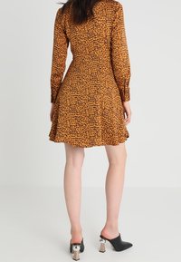 Leopardmönstrad klänning i orange och bruna nyanser med långa ärmar, utsvängd kjol och textil med struktur. Svarta högklackade mules med metalliska detaljer.