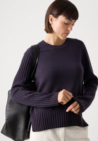 Námornícky modrý rebrovaný sveter s dlhými, textúrovanými rukávmi a okrúhlym výstrihom. V kombinácii s čiernou koženou taškou. Mäkký materiál z vlnenej zmesi.