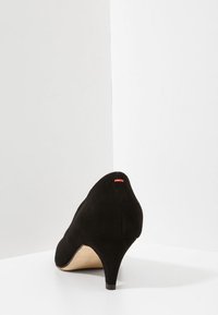 Talons en daim noir avec un bout arrondi, un talon conique de 2,5 pouces et un petit accent rouge à l'arrière. Texture lisse, design minimaliste.