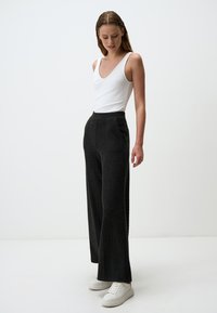 Pantaloni neri a gamba larga con un motivo testurizzato, abbinati a una canotta bianca aderente e sneakers bianche. Vestibilità comoda e vita elastica.