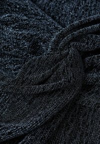 Tessuto nero testurizzato con una lucentezza metallica, caratterizzato da motivi sottili e una sensazione morbida e elastica, stratificato e piegato.