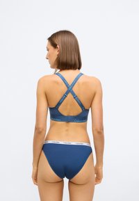 Soutien-gorge de sport bleu avec des bretelles croisées et une bande de logo ; associé à un slip de bikini bleu assorti avec une ceinture contrastante.