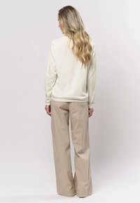 Crèmesweater met lange mouwen, gecombineerd met brede beige broek. De sweater heeft een gebreide textuur, de broek is glad en heeft een losse pasvorm.